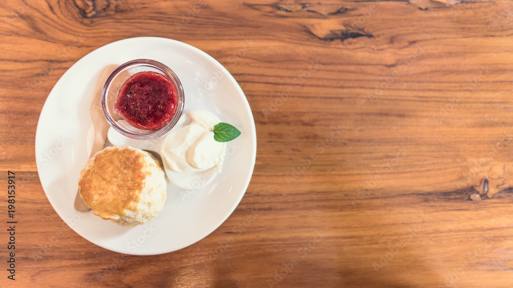 Scone with jam , clotted cream on whit plate on wooden table Scone with jam , clotted cream on whit plate on wooden table