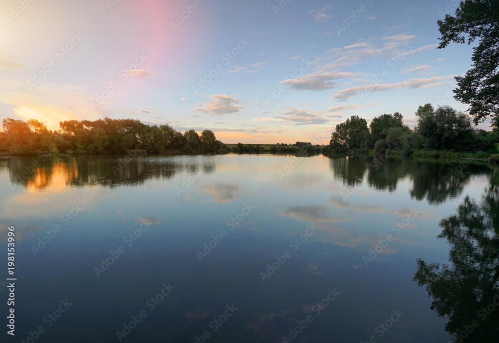 Fototapeta premium Beautiful sunset, sky with clouds above lake with trees around.
