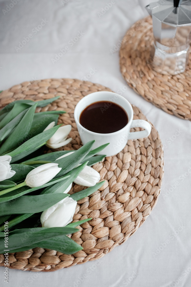A bouquet of white tulips and a cup of coffee on a table
