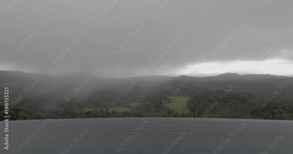 An aerial view of an infinity pool with a view of lush green and misty mountains and fields. An aerial view of an infinity pool with a view of lush green and misty mountains and fields.