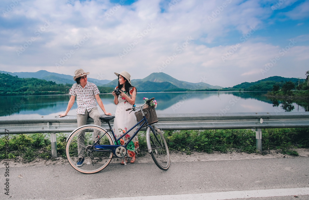 couple traveler standing beside bicycle and happy for view of nature near the lake  on vacation background is mountain.
