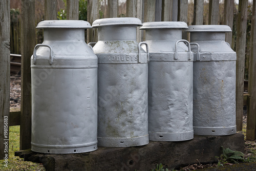 A group of four old fashioned metal milk churns showing signs of heavy usage. introduced in the 1930s held ten gallons. The use of churns ceased in Britain in 1979