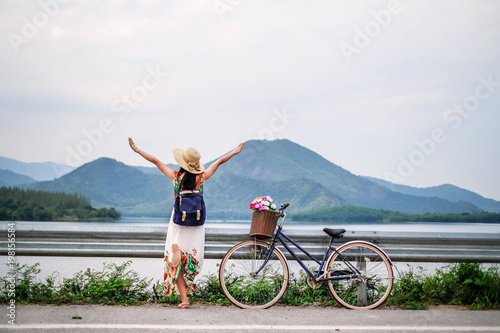 woman traveler standing beside bicycle near the lake background is mountain on vacation. young lady tourist enjoying for nature on holiday