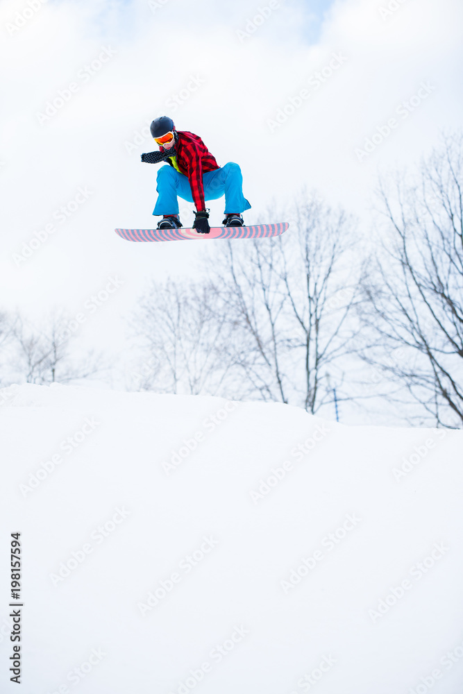 Image of athlete wearing helmet with snowboard jumping in snowy resort