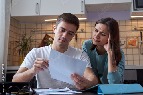 a young couple sitting at a table in the kitchen understands the finances of a young family, studying accounts and tax documents
