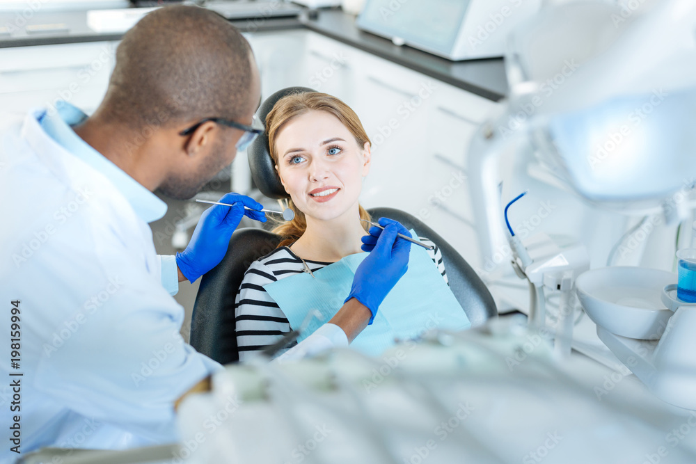 Look of gratitude. Beautiful young woman sitting in a dentist chair and smiling at her dentist while he holding a mouth mirror and a probe for a checkup Look of gratitude. Beautiful young woman sitting in a dentist chair and smiling at her dentist while he holding a mouth mirror and a probe for a checkup