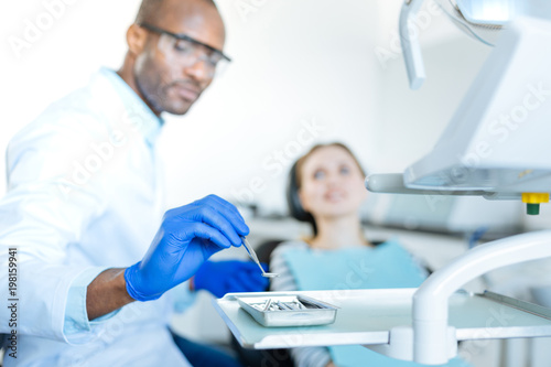 Of best quality. The focus being on the hand of a pleasant young male dentist putting a mouth mirror on a tray  having used it during the examination of his female patient