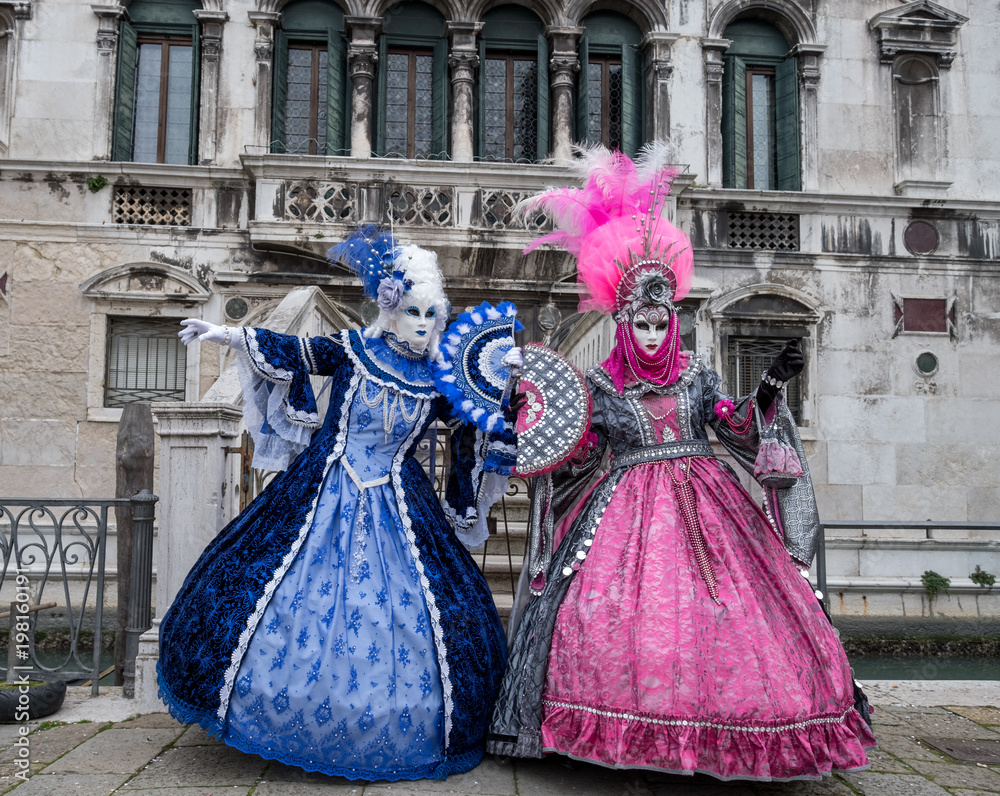 Φωτογραφία Two ladies holding fans, and wearing hand painted masks and ornate blue and pink costumes at Venice Carnival