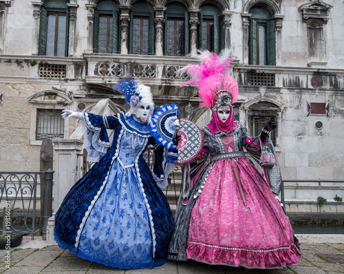 Two ladies holding fans, and wearing hand painted masks and ornate blue and pink costumes at Venice Carnival. Photographed in Campo Santa Maria Formosa.