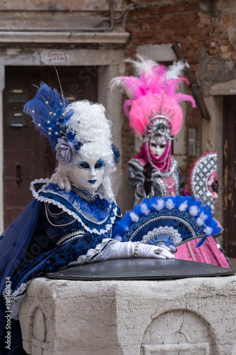 Women in costume with fans and ornate painted feathered masks at Venice Carnival. 