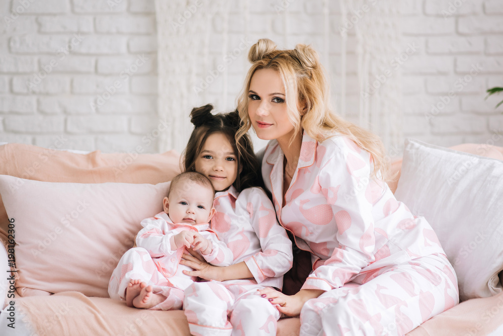 Portrait of mother with two daughters in the white room in the same pink pajamas, family look Portrait of mother with two daughters in the white room in the same pink pajamas, family look