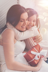 My treasure. Bright charming emotional lady sitting in bed and hugging her child tightly after she greeting her on mothers day