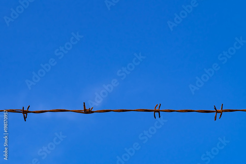 Rusty barbed wire fence against clear blue sky with copy space