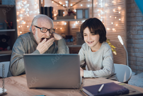 Grandfather and grandson are watching movie on laptop at night at home.