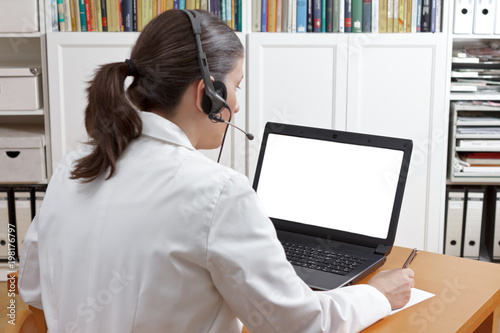 Telemedicine concept mock up: female doctor, veterinary surgeon or pharmacist with headset in front of a laptop with a blank white screen, copy space.