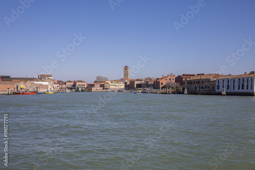 View on the island of Murano with its orange brick buildings and campanile from the Venice lagoon, Italy © Melanie