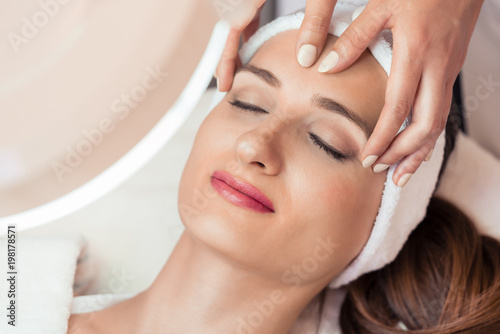 High-angle view of the face of a relaxed woman smiling under the benefits of anti-aging facial massage in a contemporary beauty center