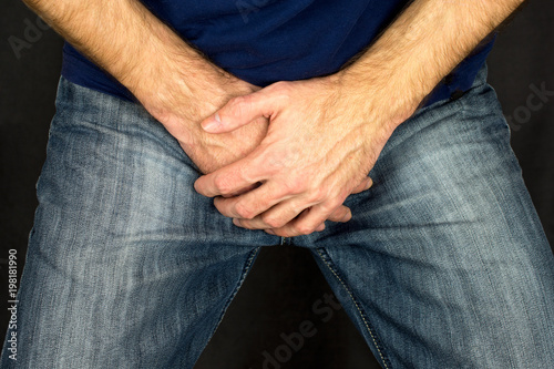  Erectile dysfunction concept. Close up of a man with hands holding his crotch dark background. Men's health. The pain from the blow in groin