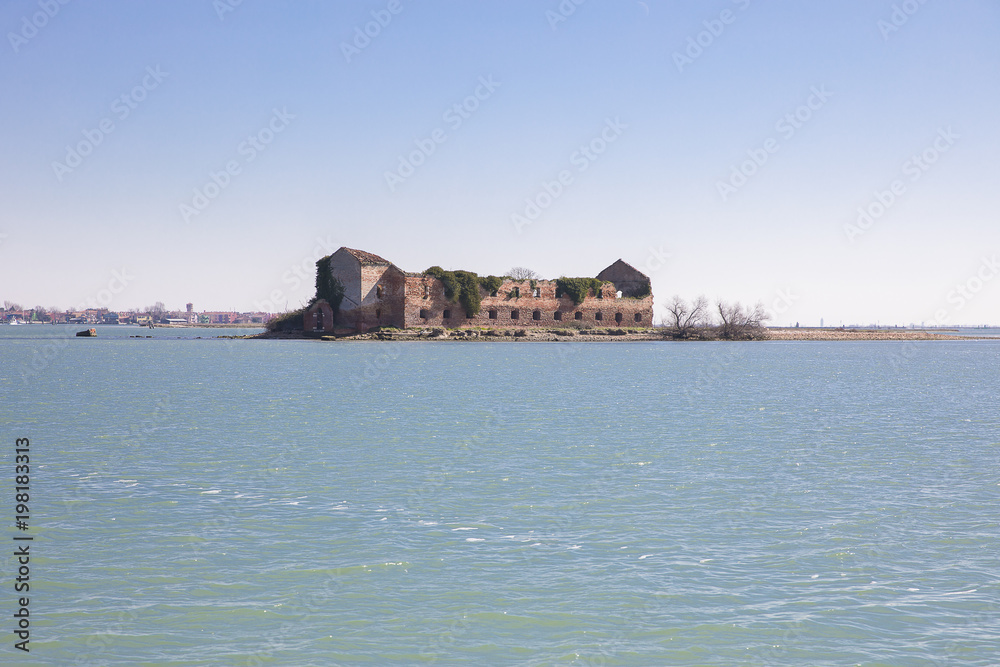 small island with old abandoned decrepit orange brick house in the lagoon of Venice near Burano, Italy