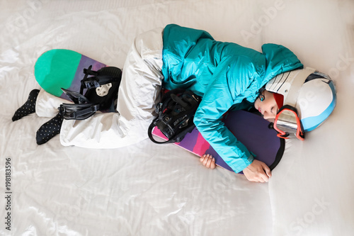 Woman in sports clothes with snowboard sleeping on bed. Winter vacation