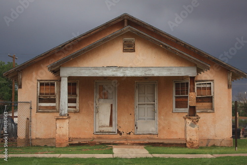 Abandoned house with weathered stucco walls, boarded-up windows, and peeling paint, set against a dark stormy sky. A glimpse into decay and forgotten architecture, captured in Tucumcari, New Mexico