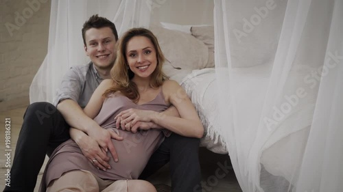 Husand is holding his wife belly. Looking at the camers photo