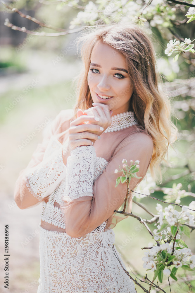 Beautiful young woman in a white romantic dress posing near blooming tree
