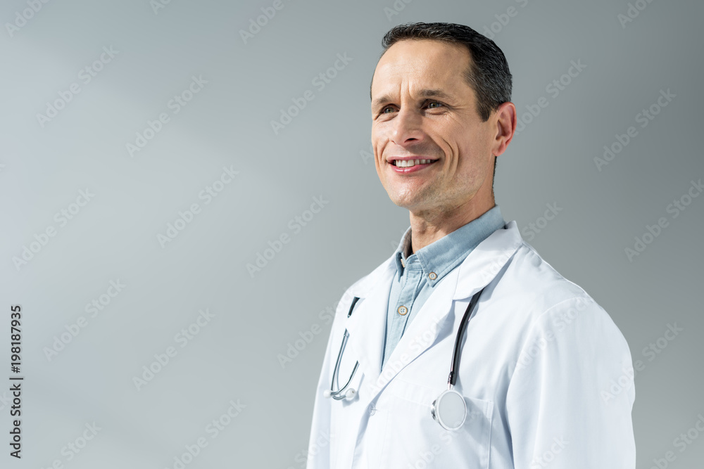handsome adult doctor in coat looking away isolated on grey handsome adult doctor in coat looking away isolated on grey