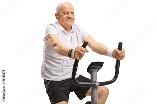 Mature man with earphones riding an exercise bike