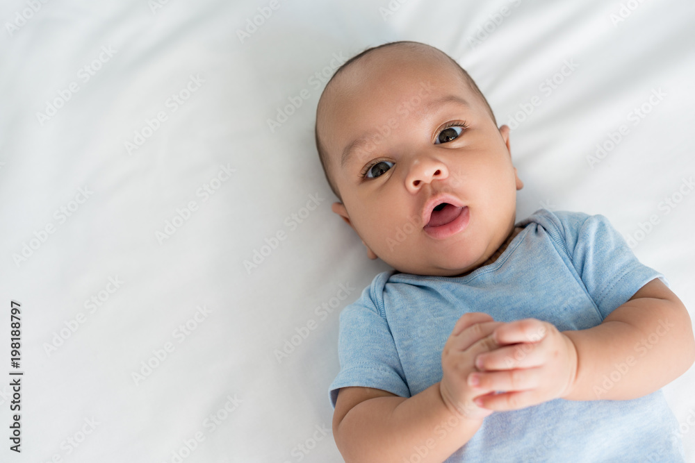 infant little baby with surprised expression looking at camera while lying in bed
