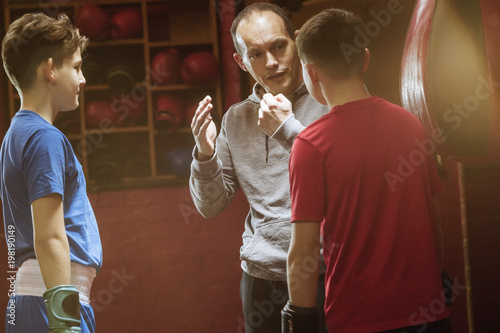 Two young boxers and male coach talk tactics in the gym before a fight