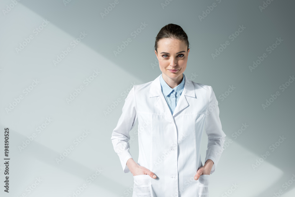 smiling female doctor in white coat looking at camera on grey smiling female doctor in white coat looking at camera on grey