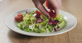 man hand adding cherry tomatoes to salad leaves