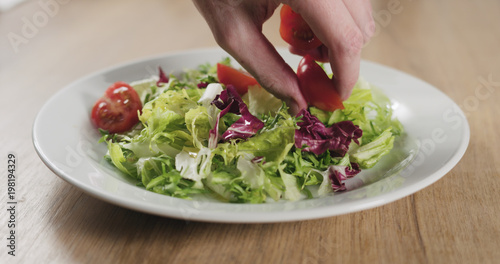 man hand adding cherry tomatoes to salad leaves
