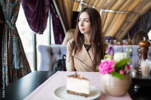 Young beautiful woman sitting in a cafe looking out the window and eating dessert.