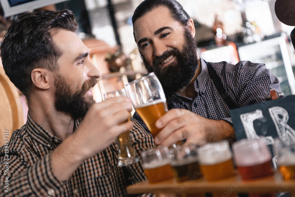 Happy bearded men try beer of different styles in beer samplers in brewery of craft beer.