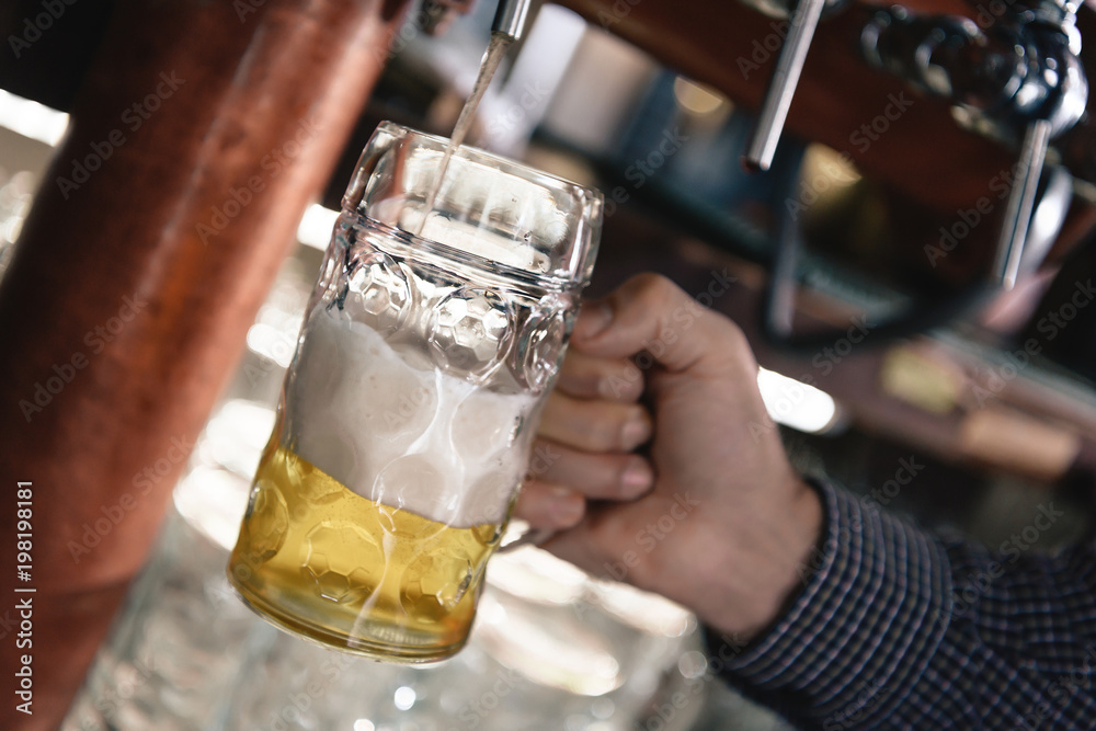 Large beer mug is filled up with beer from beer faucet. Brewer pours beer into tumbler.