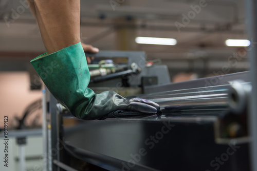 Selected focus on man hand, worker wearing a gloves clean offset printing machine after work.
