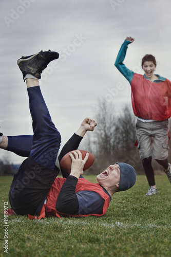 Caucasian man on the ground, punching the air, celebrating scoring points with the football in a game of non-contact flag football. photo