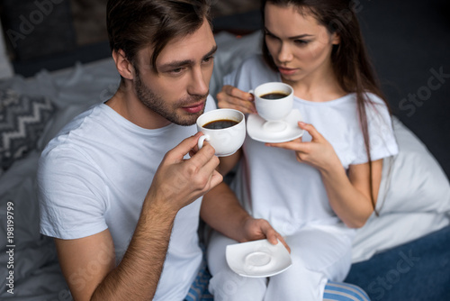 Bearded man and attractive brunette woman drinking coffee in bed