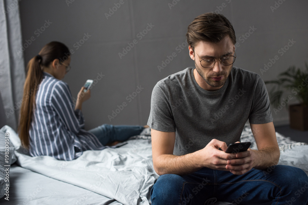 Couple in bedroom sitting on bed and using their phones Couple in bedroom sitting on bed and using their phones