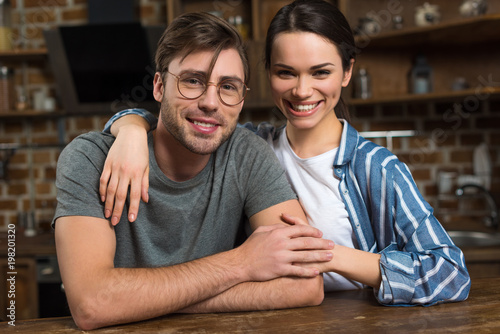 Embracing young couple sitting by table in kitchen