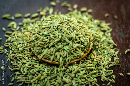 Raw dried fennel seeds or variyali or Foeniculum vulgare in a brown plate on wooden surface. photo