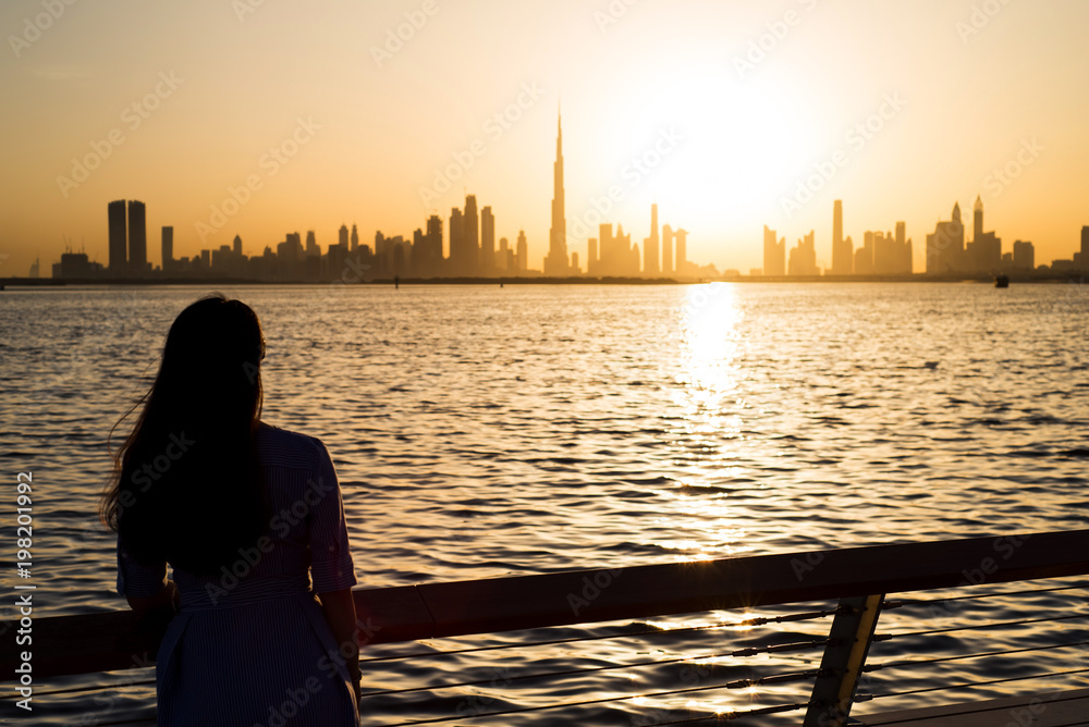 Fototapeta premium Woman facing panoramic view of Dubai at sunset