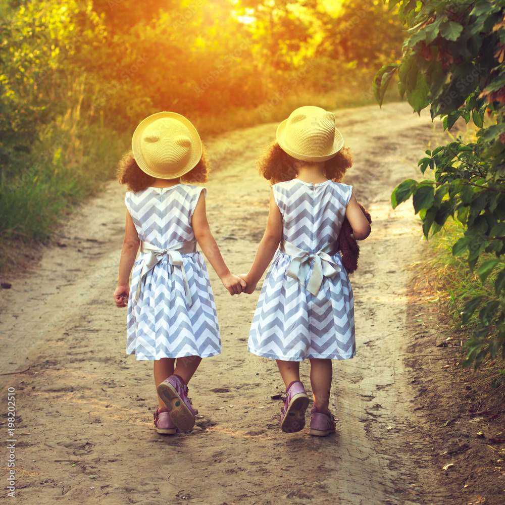 Back view of two little girls holding hand and walking together in the park in vintage color tone. Future concept Back view of two little girls holding hand and walking together in the park in vintage color tone. Future concept