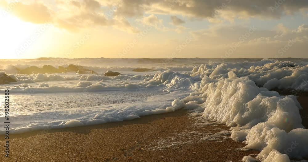 Vague d'écume de mer sur la plage au coucher du soleil