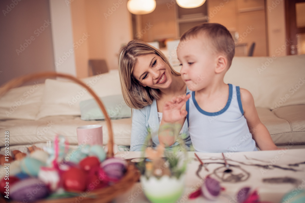 Fototapeta premium Portrait of little boy and mother coloring eggs for Easter