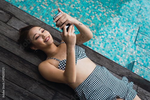 Smiling woman with smartphone relaxing at pool
