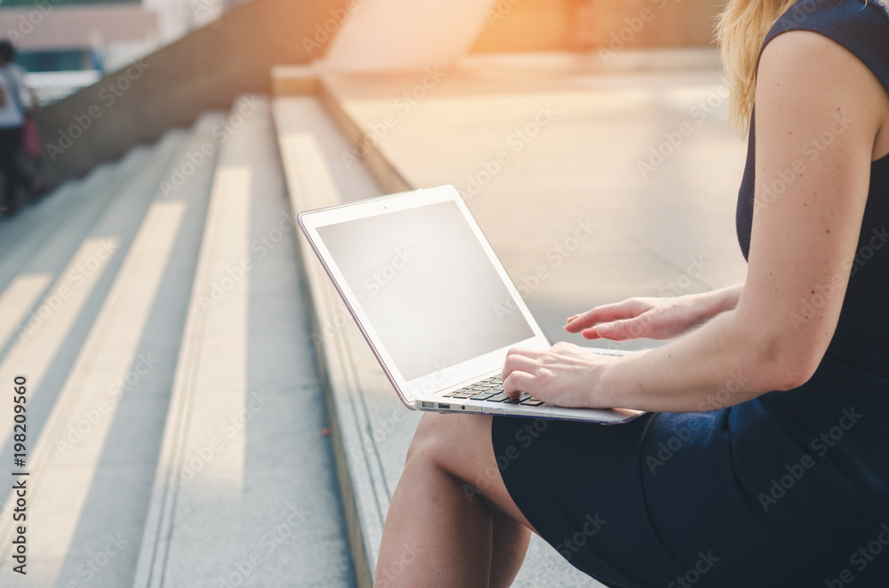 Naklejka premium attractive hand of business woman using laptop working typing key board sit on concrete stair at outdoor in the city.