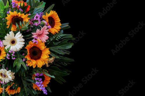 Sunflowers and Gerbera daisies flower arrangement with fern, philodendron and palm leaves the tropical foliage plants on black background.